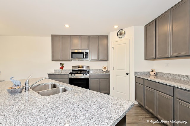 kitchen with a sink, light stone counters, stainless steel appliances, and recessed lighting