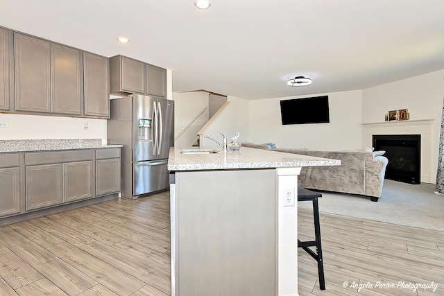 kitchen featuring stainless steel fridge, a kitchen breakfast bar, light wood finished floors, and a sink
