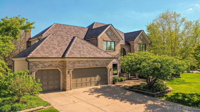 french country inspired facade with a garage, concrete driveway, brick siding, a chimney, and a front yard