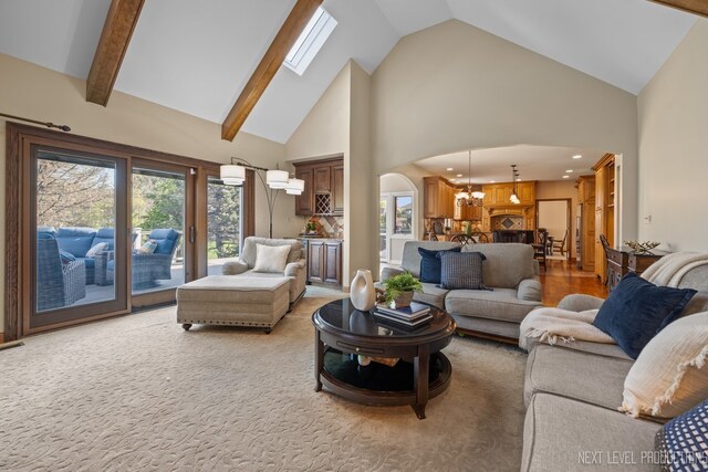 living room with high vaulted ceiling, a chandelier, arched walkways, a skylight, and light colored carpet