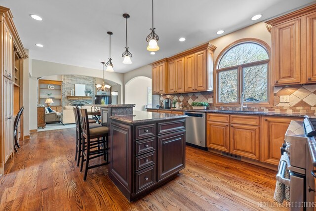 kitchen with arched walkways, stainless steel appliances, a sink, dark wood-style floors, and a breakfast bar