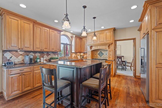 kitchen featuring stainless steel fridge with ice dispenser, a kitchen island, a kitchen breakfast bar, recessed lighting, and dark stone counters