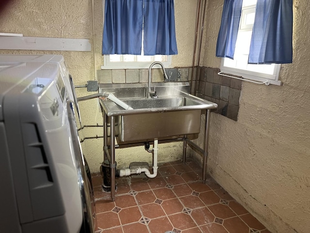 laundry room with a textured wall, independent washer and dryer, and dark tile patterned flooring