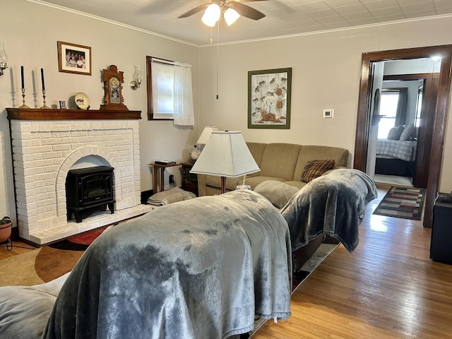 living area with ceiling fan, ornamental molding, wood finished floors, and a wood stove