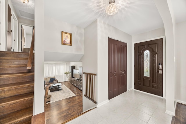 entrance foyer featuring an inviting chandelier, stairs, baseboards, tile patterned floors, and arched walkways