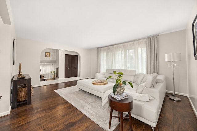 living room with arched walkways, baseboards, and wood finished floors