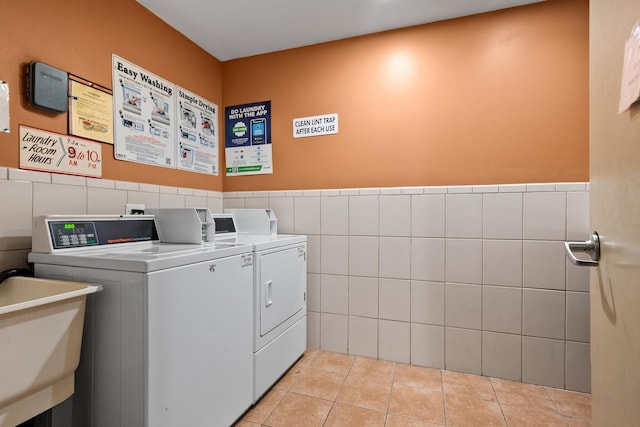 community laundry room featuring light tile patterned floors, a sink, a wainscoted wall, tile walls, and washer and clothes dryer