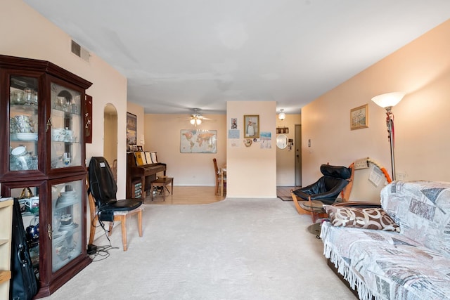 living area featuring baseboards, ceiling fan, visible vents, and light colored carpet