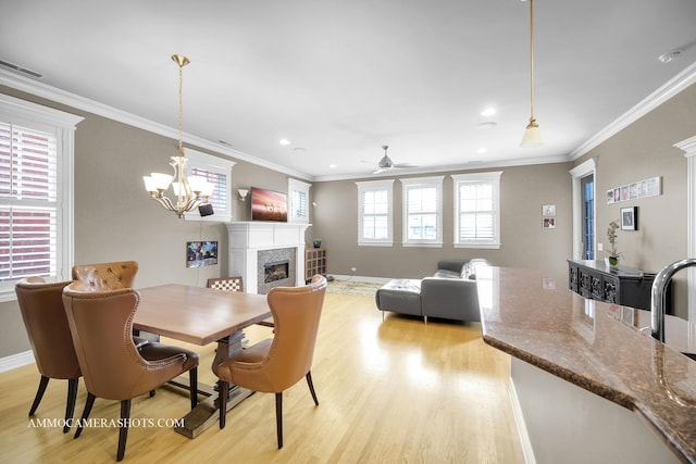 dining space with crown molding, a fireplace, light wood-type flooring, baseboards, and ceiling fan with notable chandelier