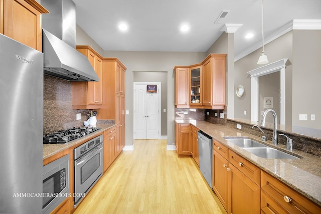 kitchen with decorative backsplash, wall chimney range hood, light stone counters, a sink, and stainless steel appliances