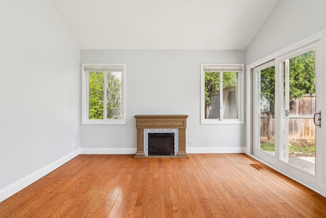 unfurnished living room featuring vaulted ceiling, baseboards, light wood-type flooring, and a fireplace with raised hearth