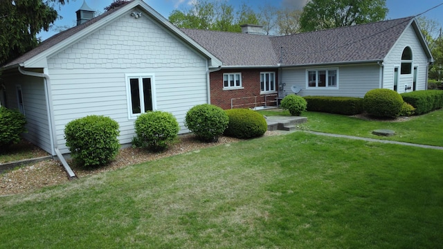 back of house featuring a shingled roof, a chimney, and a lawn