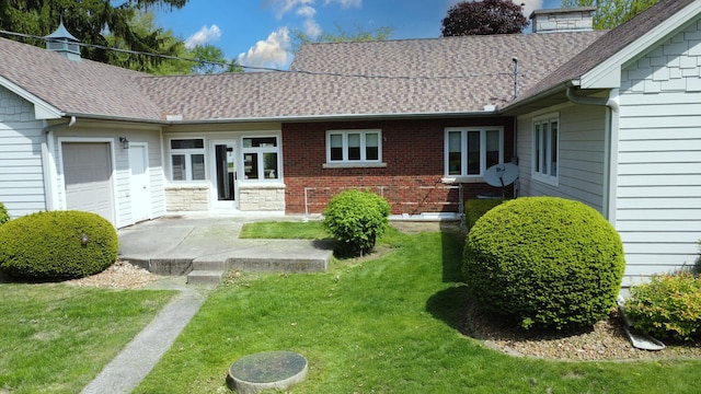 back of property with an attached garage, roof with shingles, a chimney, and a lawn