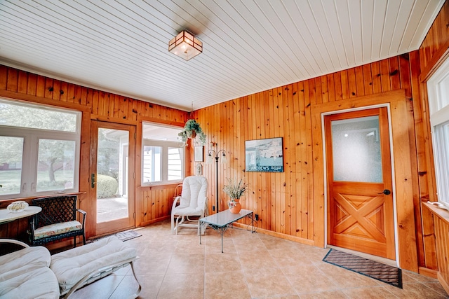 living area featuring light tile patterned floors, wood walls, and baseboards