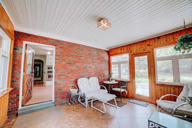 sunroom / solarium featuring wood walls, tile patterned flooring, and brick wall