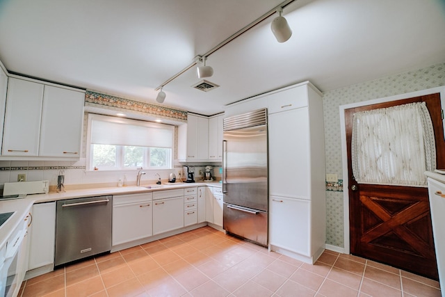 kitchen featuring wallpapered walls, a sink, track lighting, light countertops, and appliances with stainless steel finishes