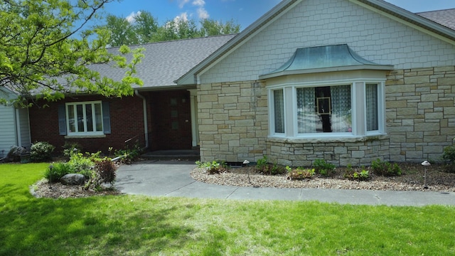 view of front of home featuring roof with shingles, stone siding, and a front yard