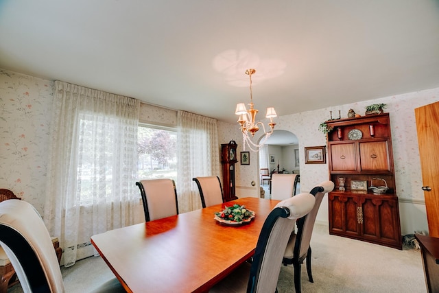 dining space with light carpet, a notable chandelier, arched walkways, and wallpapered walls