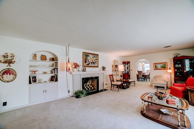 living area featuring carpet flooring, a fireplace with flush hearth, built in features, visible vents, and arched walkways