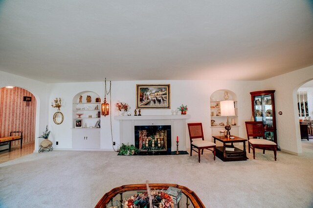 carpeted living room with arched walkways, baseboards, a fireplace with flush hearth, and built in shelves