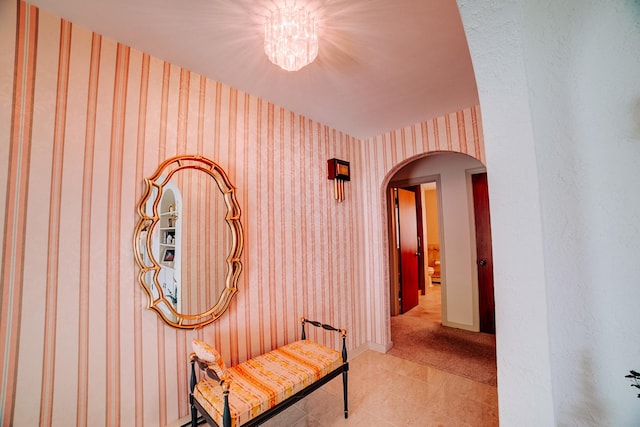 corridor with wallpapered walls, light carpet, baseboards, arched walkways, and a chandelier