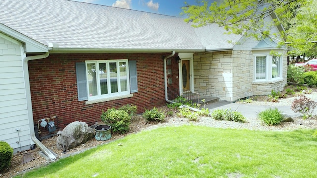 property entrance featuring a yard, roof with shingles, and stone siding