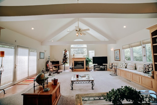 living area with lofted ceiling with beams, a healthy amount of sunlight, a glass covered fireplace, and ceiling fan
