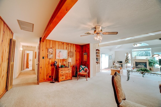 interior space with light colored carpet, wood walls, beamed ceiling, and a glass covered fireplace
