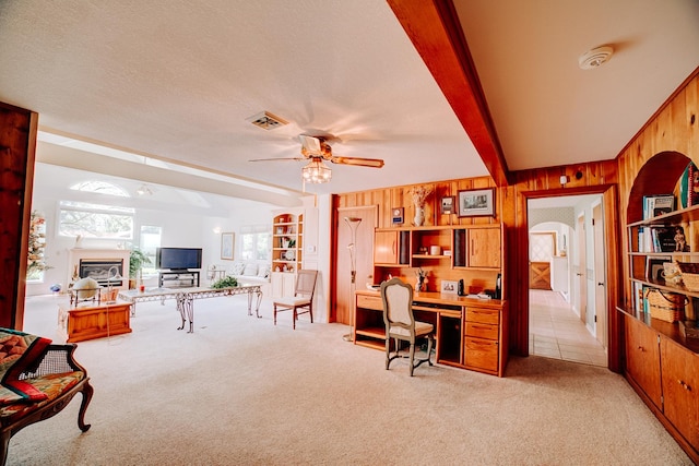 home office featuring visible vents, light carpet, wooden walls, arched walkways, and a ceiling fan