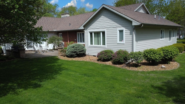 rear view of property with a patio, roof with shingles, a chimney, and a lawn