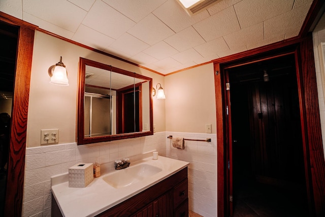 full bathroom with tile walls, a wainscoted wall, vanity, ornamental molding, and a stall shower