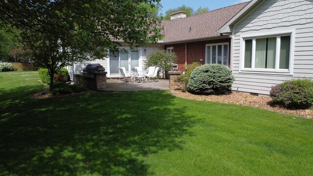 exterior space with roof with shingles, crawl space, a yard, a patio, and a chimney