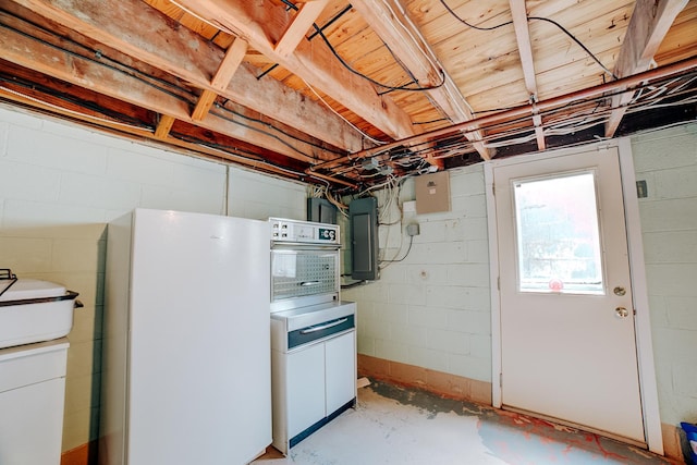basement featuring electric panel, freestanding refrigerator, and concrete block wall