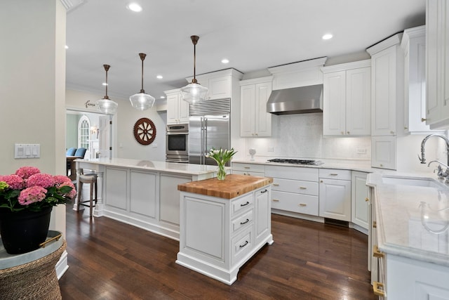 kitchen featuring built in fridge, wall chimney exhaust hood, a sink, a center island, and wood counters
