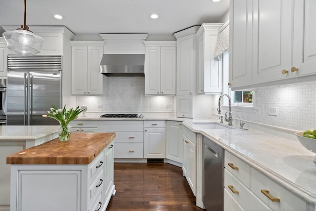 kitchen featuring stainless steel appliances, a sink, wood counters, wall chimney range hood, and recessed lighting