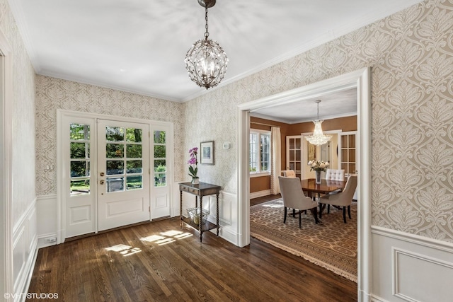entrance foyer with a chandelier, wallpapered walls, ornamental molding, and dark wood-type flooring