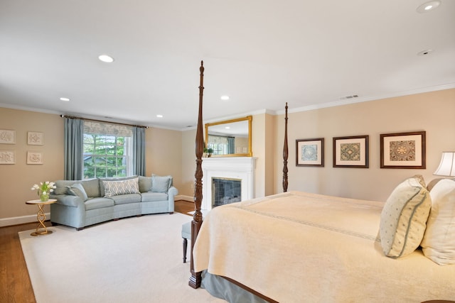 bedroom with wood finished floors, ornamental molding, baseboards, recessed lighting, and a glass covered fireplace