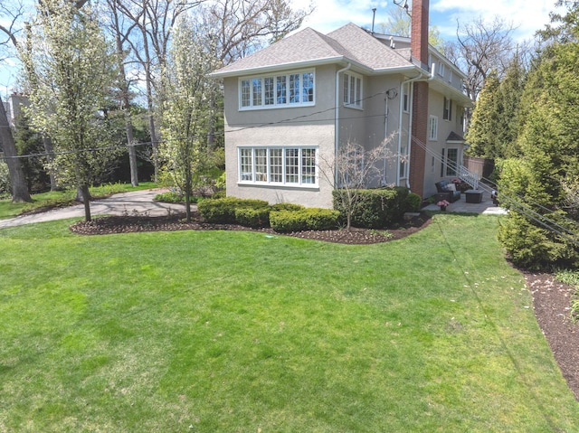view of side of property with a lawn, stucco siding, a chimney, and roof with shingles