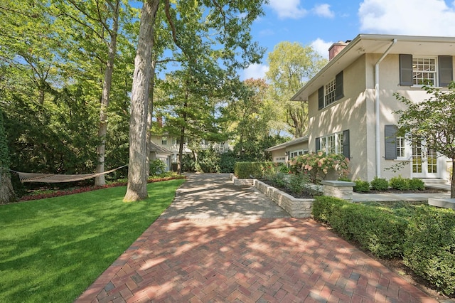 view of side of property featuring stucco siding, french doors, a chimney, and a lawn