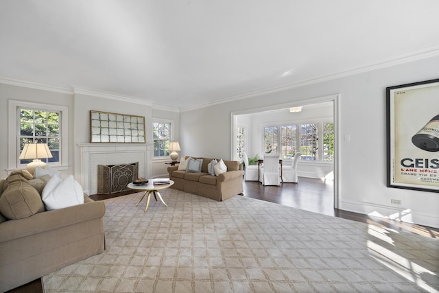 living room with crown molding, plenty of natural light, a brick fireplace, wood finished floors, and baseboards