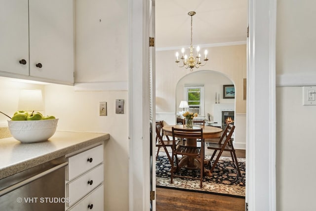625 Greenbriar Ln, Lake Forest, IL 60045 - dining space with crown molding, a chandelier, a warm lit fireplace, arched walkways, and dark wood-style floors