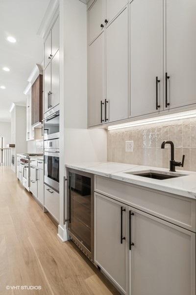 1928 W George St, Chicago, IL 60657 - kitchen with wine cooler, light wood-style floors, backsplash, light stone countertops, and recessed lighting