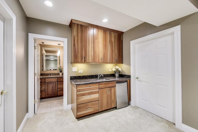 kitchen with stainless steel dishwasher, a sink, light carpet, brown cabinetry, and dark stone counters