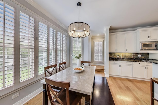 dining space featuring light wood-style floors, a chandelier, crown molding, and baseboards
