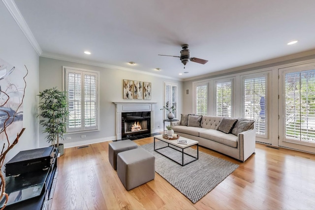 living area featuring healthy amount of natural light, crown molding, wood finished floors, a fireplace with flush hearth, and ceiling fan