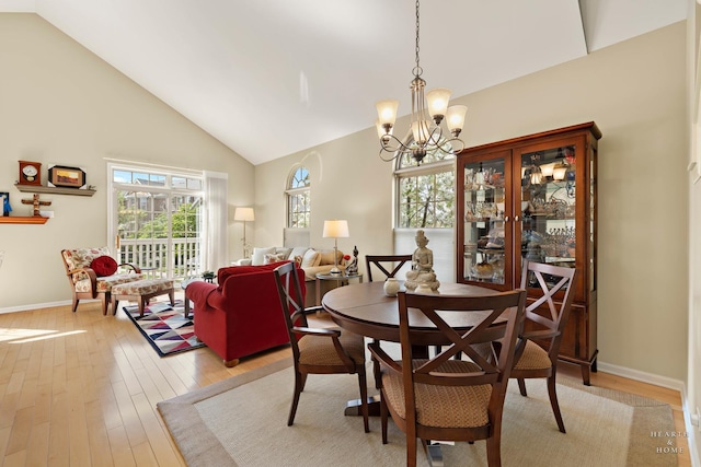 dining area with a chandelier, high vaulted ceiling, light wood-style flooring, and baseboards