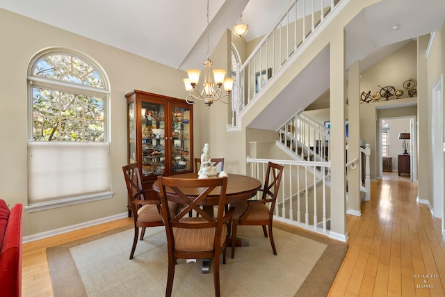 dining room featuring light wood-style floors, a chandelier, stairs, baseboards, and high vaulted ceiling