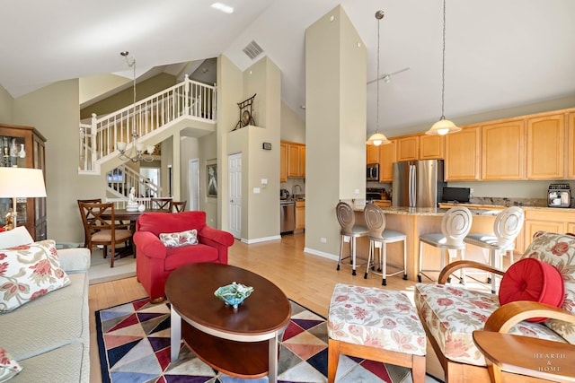 living area with stairway, light wood finished floors, and high vaulted ceiling