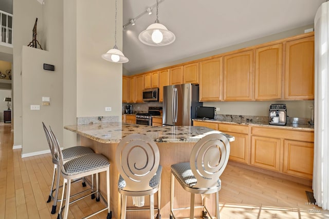 kitchen with appliances with stainless steel finishes, light wood finished floors, a kitchen bar, light stone counters, and a towering ceiling