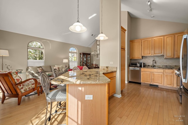 kitchen featuring dishwasher, a peninsula, light wood-style flooring, open floor plan, and a breakfast bar